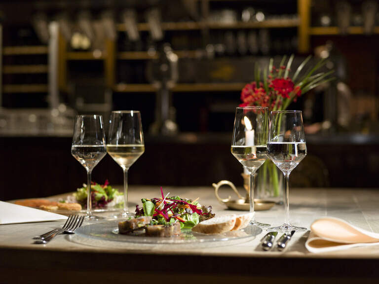 Modern gedeckter Tisch mit einem Gericht bestehend aus Salat mit Gläsern und Blumen im Hintergrund.
